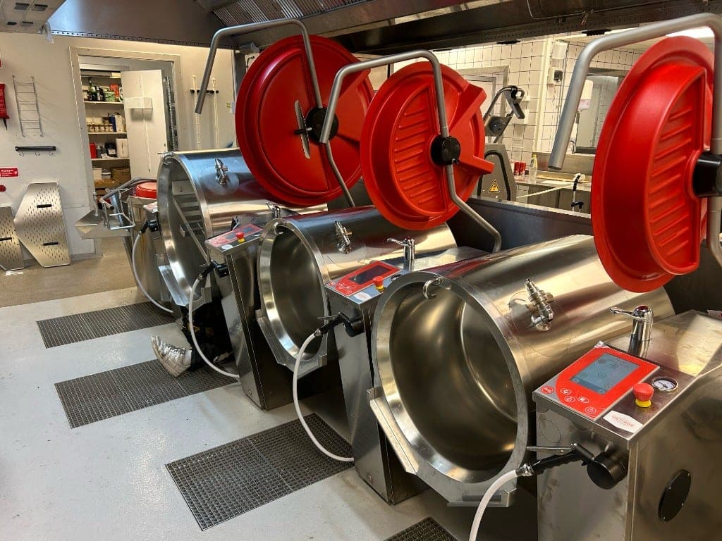 Tre nyinstallerade kokgrytor med röda lock i ett storkök